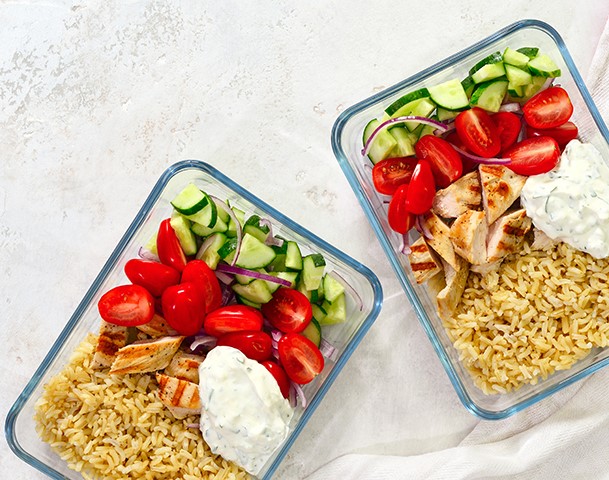 Greek style grilled chicken breasts with tzatziki and freshly diced vegetables prepared and ready to eat in a take away lunch boxes, view from above, space for a text